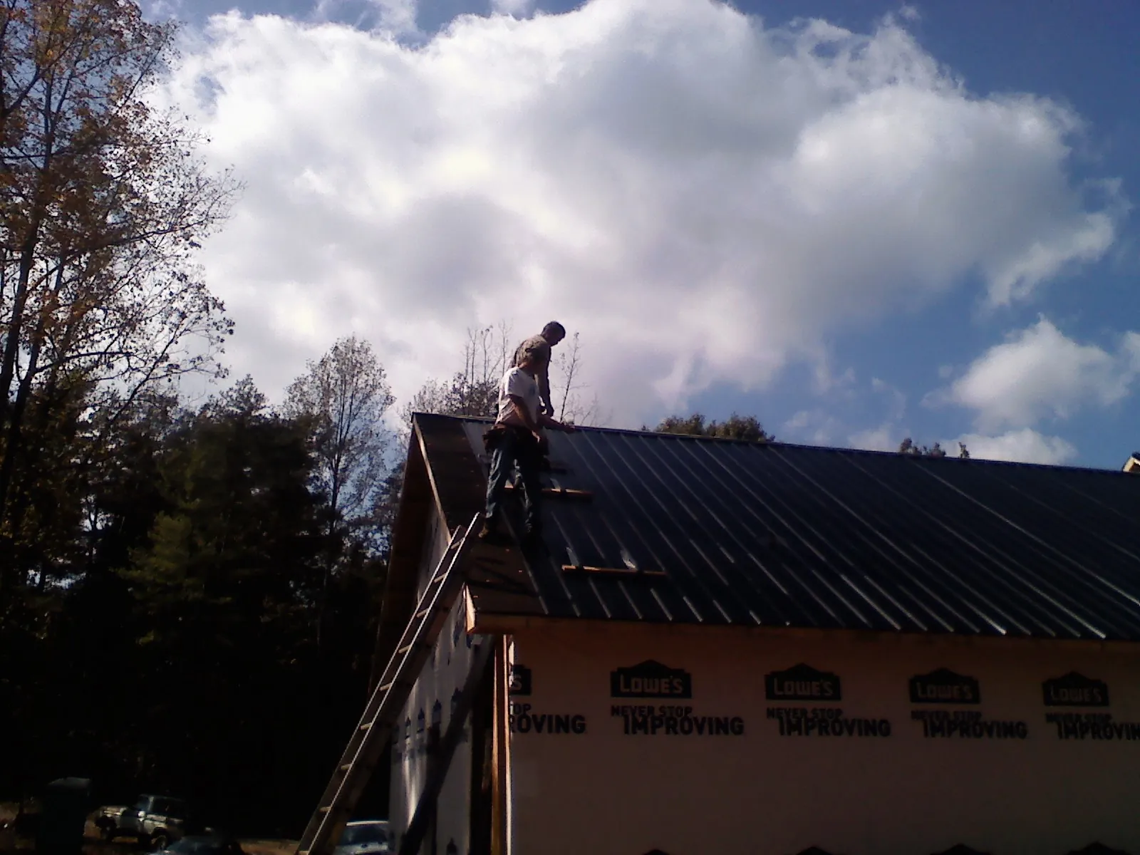 Roofer fastening dark metal panels high against a cloudy sky, from a Roof Inspection job in Mount Vernon
